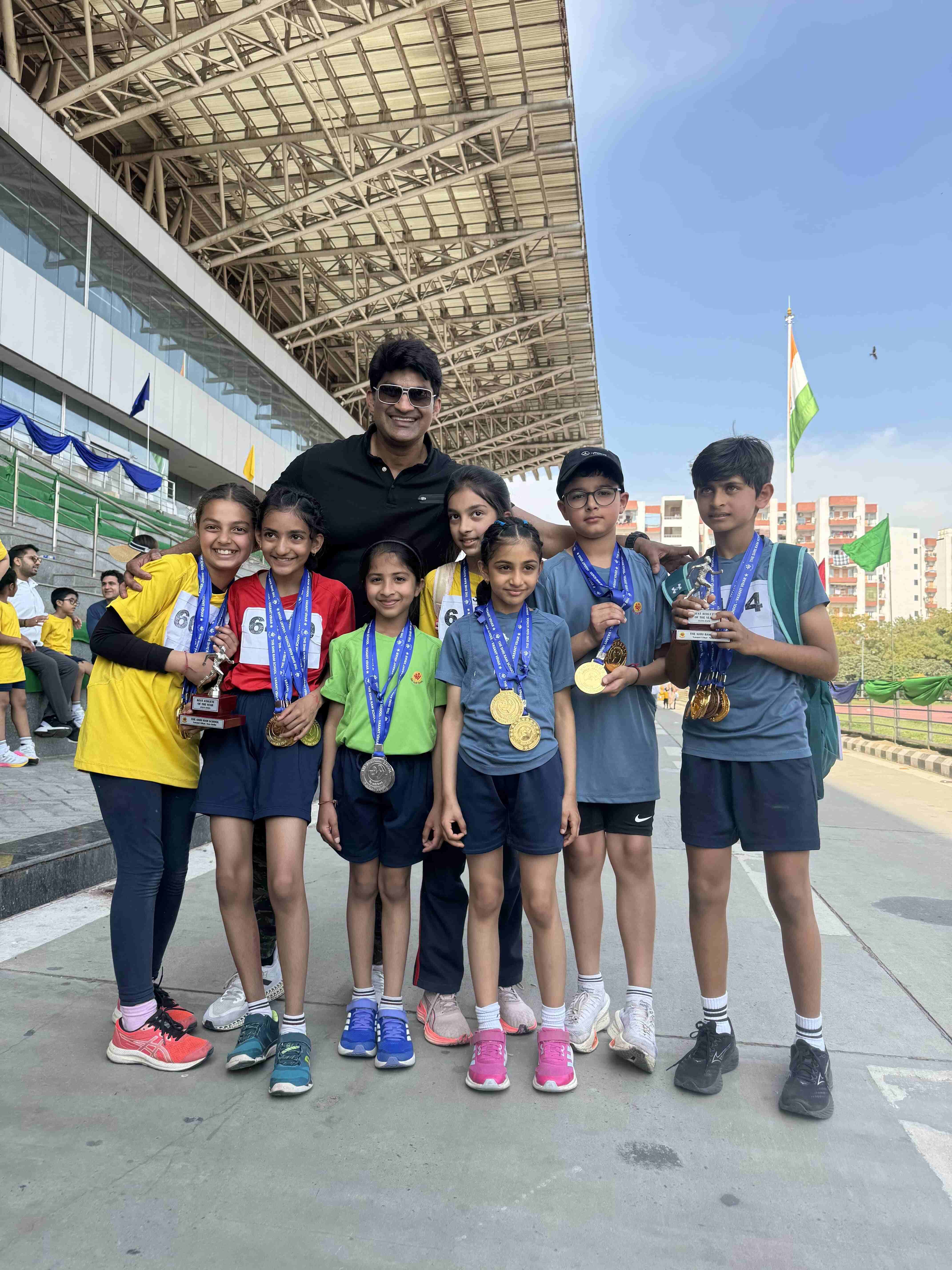 Young athletes with coach at medal ceremony, wearing medals and holding trophies after successful competition at stadium